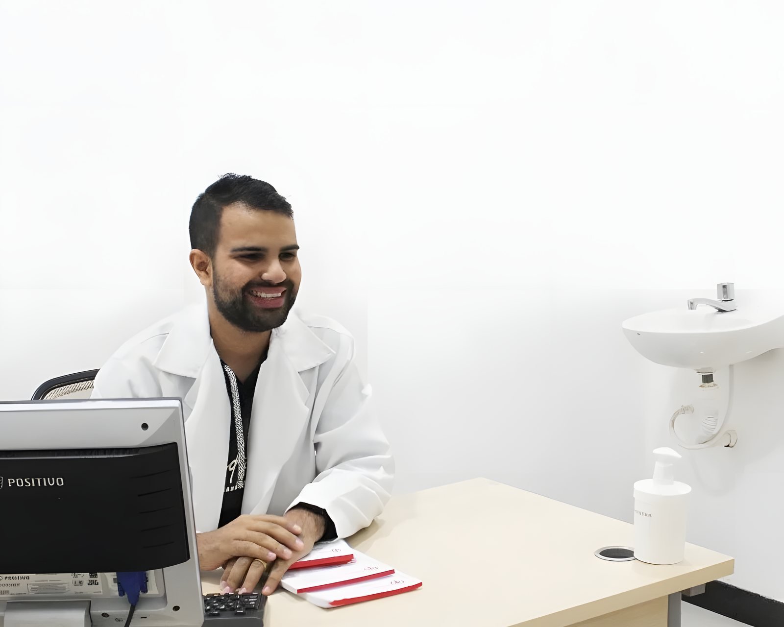 Guilherme Eduardo de jaleco branco, sorrindo, no balcão de atendimento da farmácia