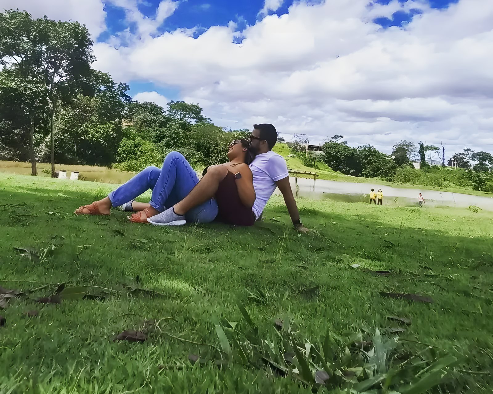 Guilherme Eduardo e a esposa sentados na grama de um parque, em um dia de sol